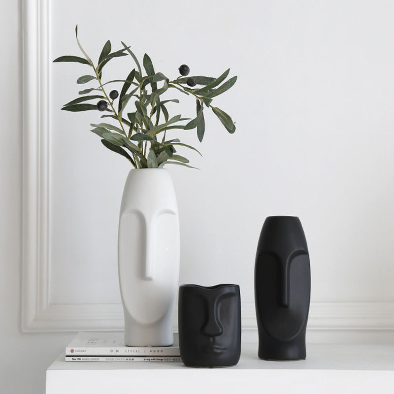 White Nordic ceramic face-art vase holding an olive branch