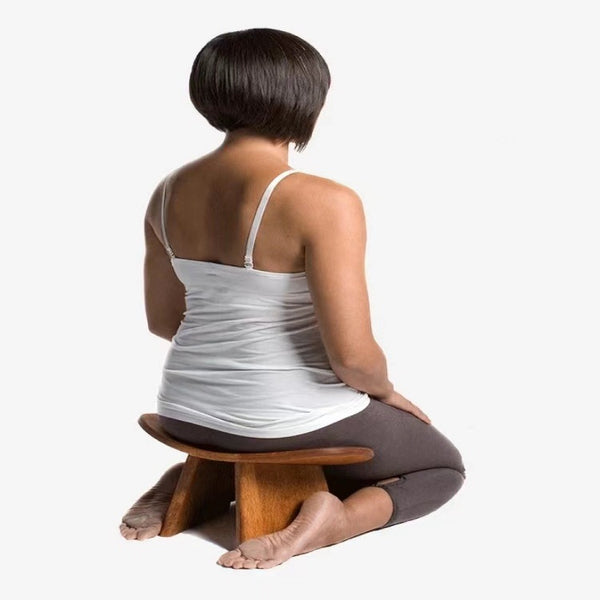 Person kneeling in meditation posture on a solid wood kneeling stool bench