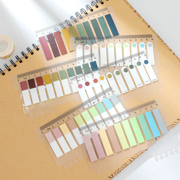 Pastel-colored sticky note index tabs with ruler markings on a spiral notebook