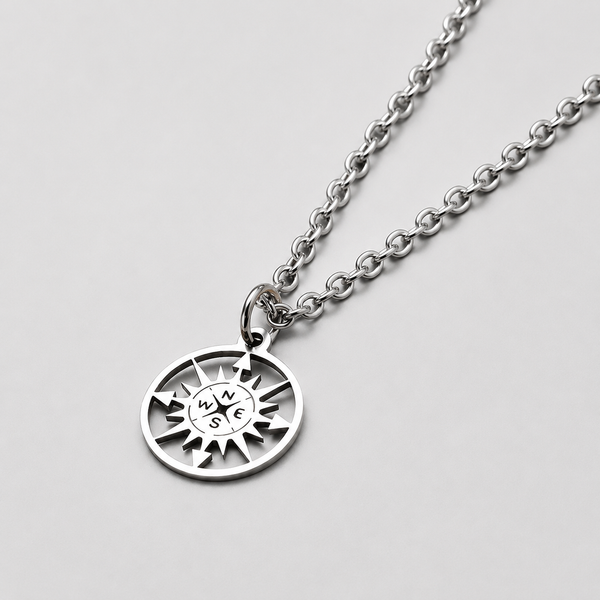 Close-up of the stainless steel necklace's compass pendant, chain draped across a flat surface