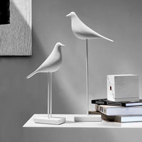 Pair of modern minimalist white bird figurines on stands, displayed on a shelf